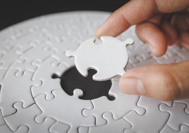 A person completing a jigsaw puzzle by placing the last piece in the centre. Image by Tinnakorn jorruang via Shutterstock.