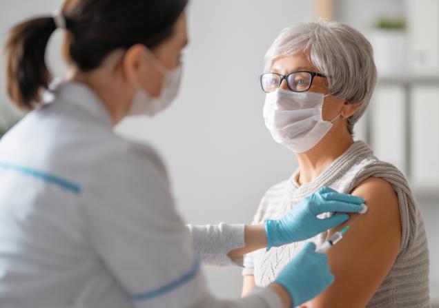 A doctor giving a senior woman a vaccination. They are both wearing facemasks. Image by Yuganov Konstantin via Shutterstock.