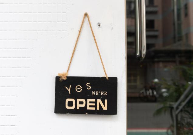 Sign hanging on a board that reads 'Yes we're open'. Image by Robbin Lee via Shutterstock