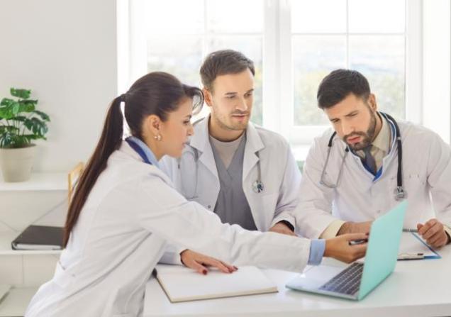 Three doctors discussing around a laptop. COMPASS aims to boost cardiology-oncology collaboration.