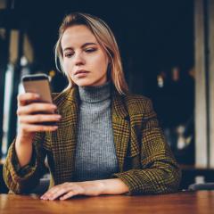IMI projects are using smartphone apps to gather real time, reliable information on patients' health. Image by GaudiLab via Shutterstock. A young woman with a serious expression on her face is sitting at a table, using a smartphone. Image by GaudiLab via Shutterstock.
