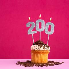 Image by Luis Echeverri Urrea via Shutterstock. A birthday cupcake with lit silver candles saying '200'. The cupcake has white icing and chocolate sprinkles. The background of the image is pink. Image by Luis Echeverri Urrea via Shutterstock.