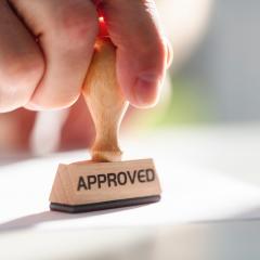 A hand stamping something with an 'APPROVED' stamp. Image by Brian A Jackson via Shutterstock.