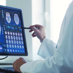 A doctor looking at a brain scan on a screen. Image by Max Acronym via Shutterstock