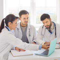 Three doctors discussing around a laptop. COMPASS aims to boost cardiology-oncology collaboration.