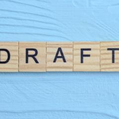 The word DRAFT written on wooden blocks on a pale blue background. Image by Butus via Shutterstock.