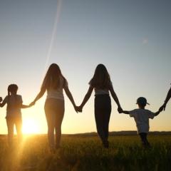 A group of people of all ages standing before a sunset. 