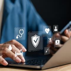 A person typing on a laptop. Health icons float above their hands, symbolising health data sharing.