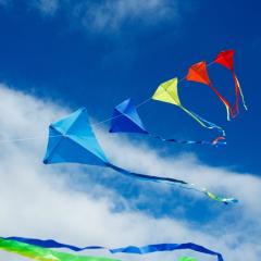 A string of coloured kites flying high against a blue sky with a few white clouds. Image by Sergey Novikov via Shutterstock.
