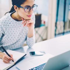 A woman looking at a computer screen and taking notes. 