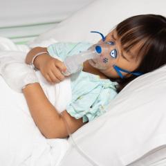 A young girl lying in a hospital bed with her eyes closed and an oxygen mask on. Image by Huttsu via Shutterstock.