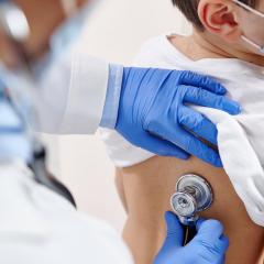 A doctor listens to a child's lungs via a stethoscope. Image by Taras Grebinets via Shutterstock