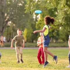 A group of 5 children playing frisbee in a park on a sunny day. Image by New Africa via Shutterstock.