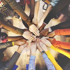 Multiple people's hands reaching together as viewed from above. Image by Rawpixel.com via Shutterstock