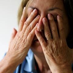 A tired woman rubs her eyes and face with her fingers. She has tanned skin, dark blond hair and a blue shirt. Image by Bricolage via Shutterstock