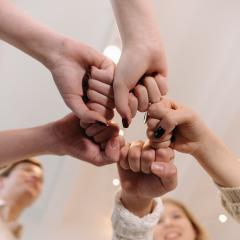 Five hands viewed from below doing a fist bump. Image by Pavel Danilyuk via Pexels.
