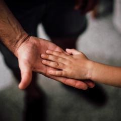 A child places their left hand on the upturned palm of a man's right hand. Image by Juan Pablo Serrano Arenas via Pexels.