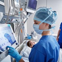 A healthcare worker working at a machine in an intensive care unit. Image by Peakstock via Shutterstock.