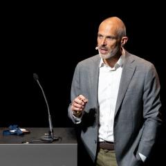 Niklas Blomberg speaking at an event last year. Image courtesy of ELIXIR. Niklas Blomberg speaking at an event last year. He is wearing a grey jacket and white shirt and is standing next to a black lectern with a microphone on it. Image courtesy of ELIXIR.