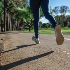 The legs of a person jogging. They're wearing blue leggings and trainers and they're jogging along a road with grass on the right and trees on the left. Image by Daniel Reche via Pexels