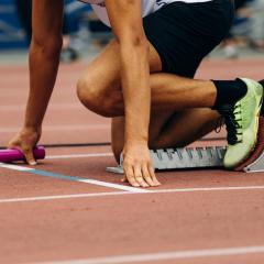 A sprinter at the start of a relay race. Their shoes are bright yellow/green and the baton is pink