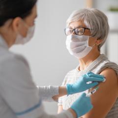 A doctor giving a senior woman a vaccination. They are both wearing facemasks. Image by Yuganov Konstantin via Shutterstock.