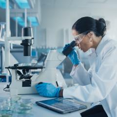 Woman looking down a microscope in the lab. Image by Gorodenkoff via Shutterstock